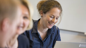 Three people in a classroom, taking a course.