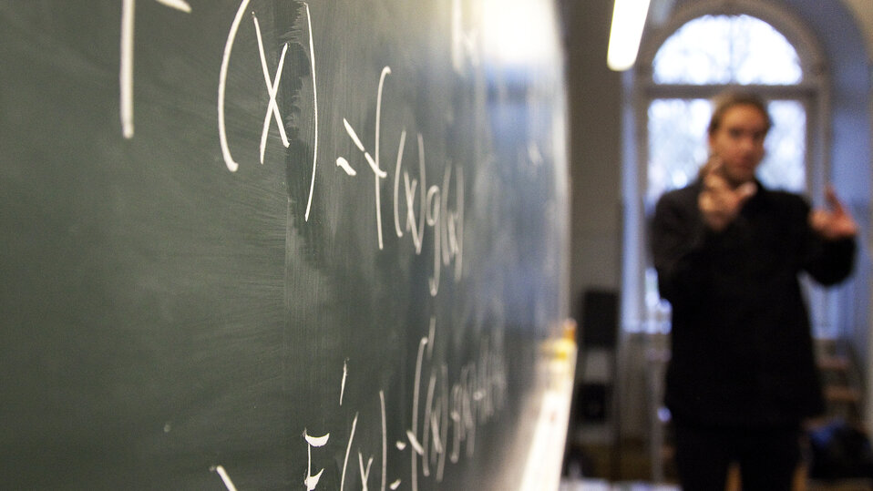 En matematiklärare vid en svart tavla med matematiska tecken på.